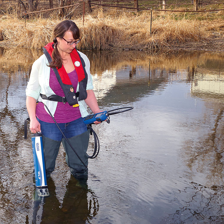 A hydrologist spot sampling with a HL7 sonde and reading data with a surveyor in a body of water.