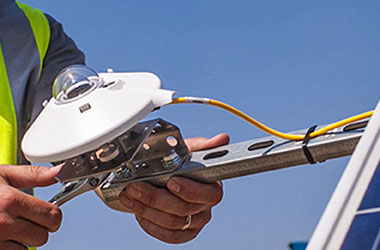 A close up of a site technician’s hands loosening the mounting bracket of a pyranometer to perform maintenance.