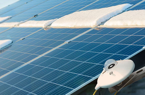 A Kipp & Zonen pyranometer mounted beside an angled, partly snow-covered solar panel.